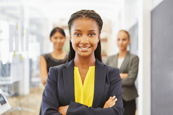 Apprenticeship scheme - happy employees. Lady in suit in office forefront of camera, with two ladies dressed smartly behind